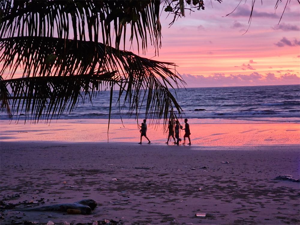 People walking on Klong Dao Beach at sunset
