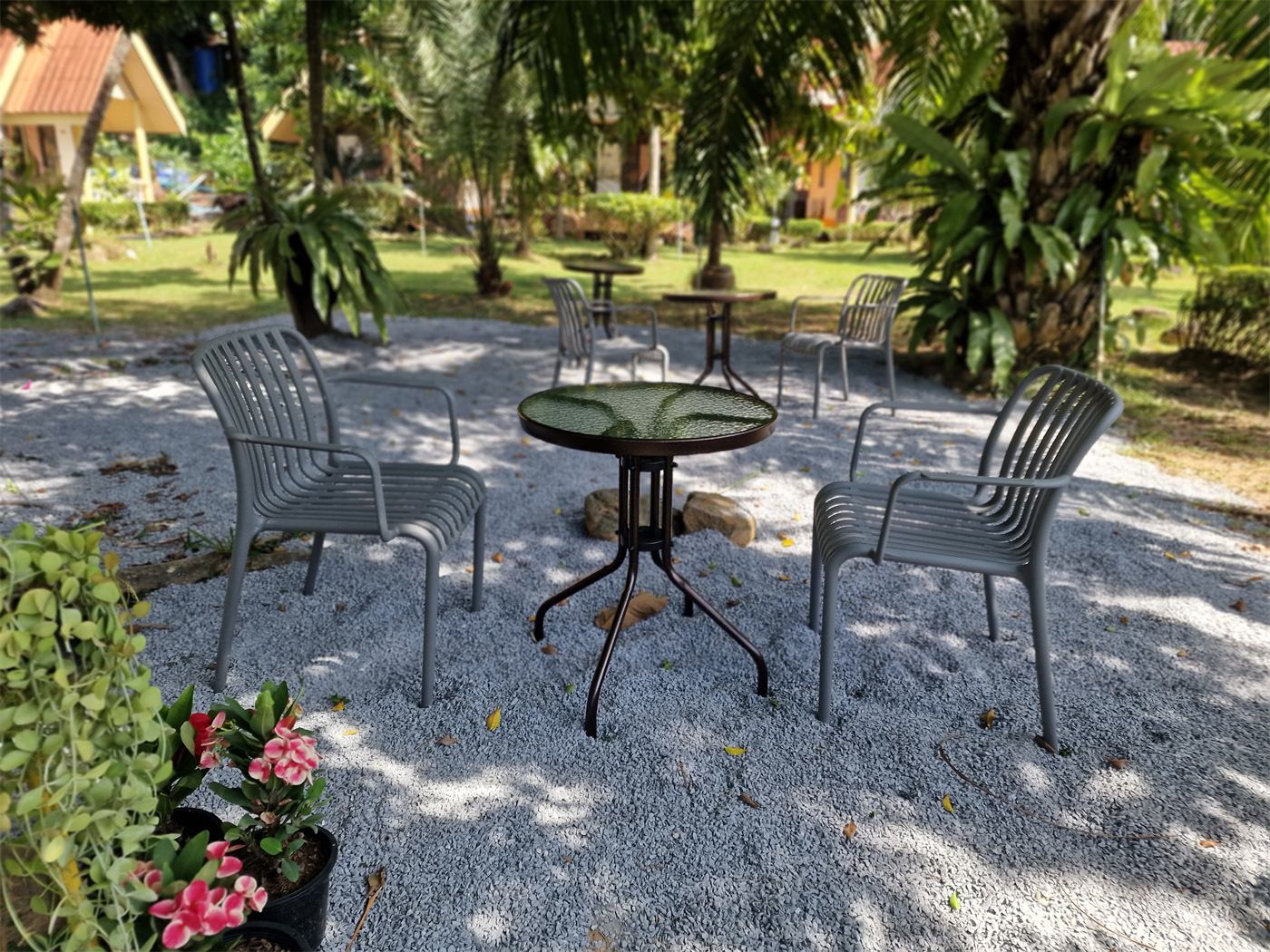 Tables and chairs on white gravel under the trees, with pink flowers